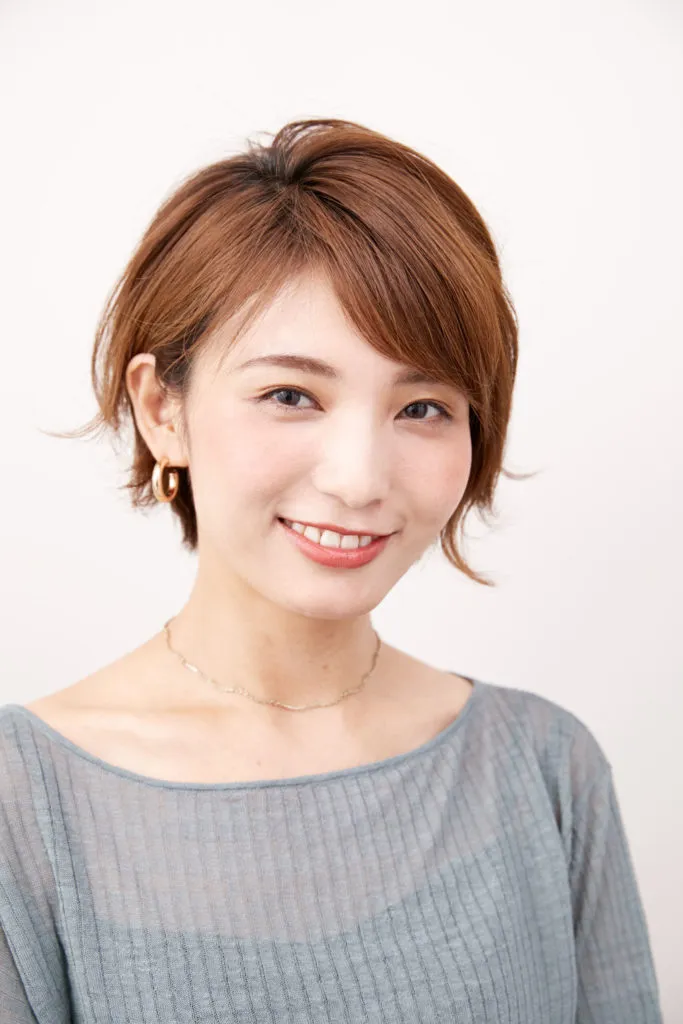 ショートヘアから伸ばしかけの女性が、ストレートアイロンを使って表面に外ハネっぽい動きを出している写真