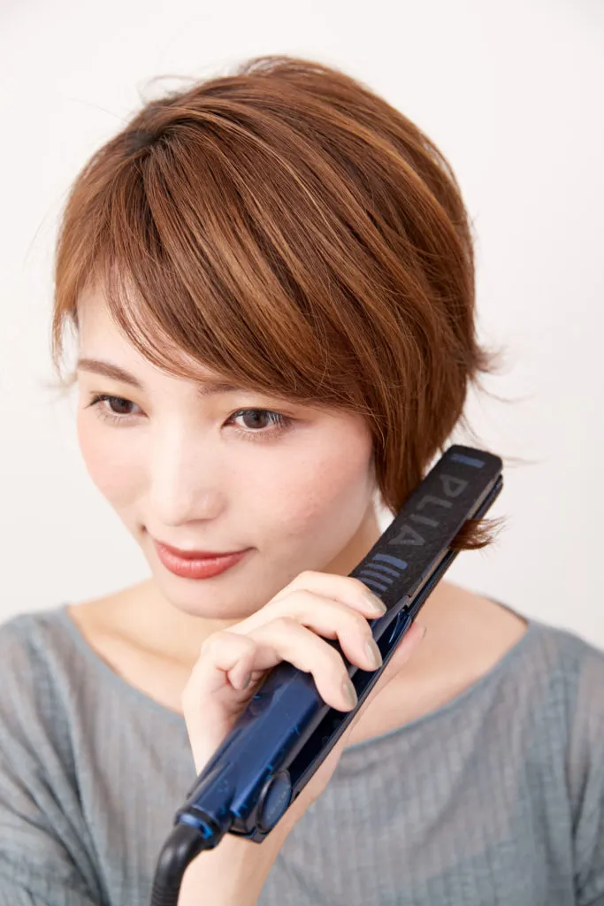 ショートヘアから伸ばしかけの女性がストレートアイロンで毛先を外ハネにしている様子