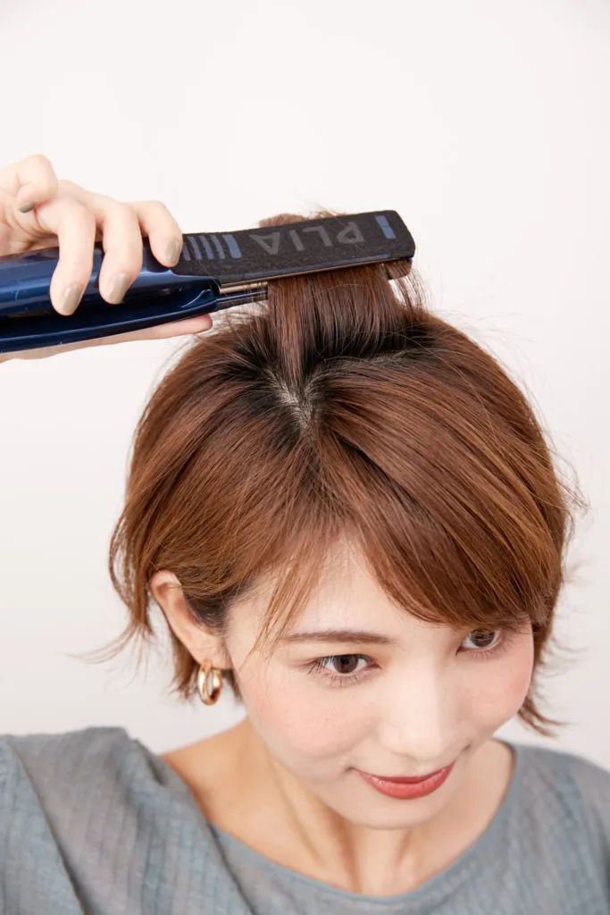ショートヘアから伸ばしかけの女性がストレートアイロンでトップを外ハネにしている様子