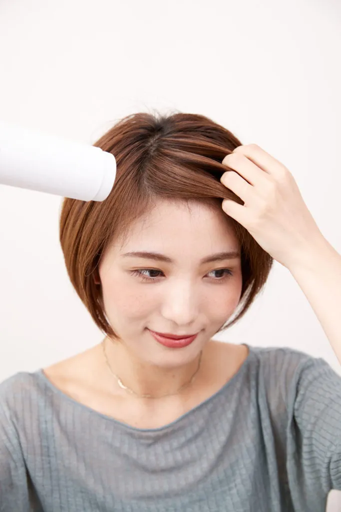 ショートヘアから伸ばしかけの女性が普段の分け目にドライヤーを当てて手ぐしでドライしてヘアアレンジをしている