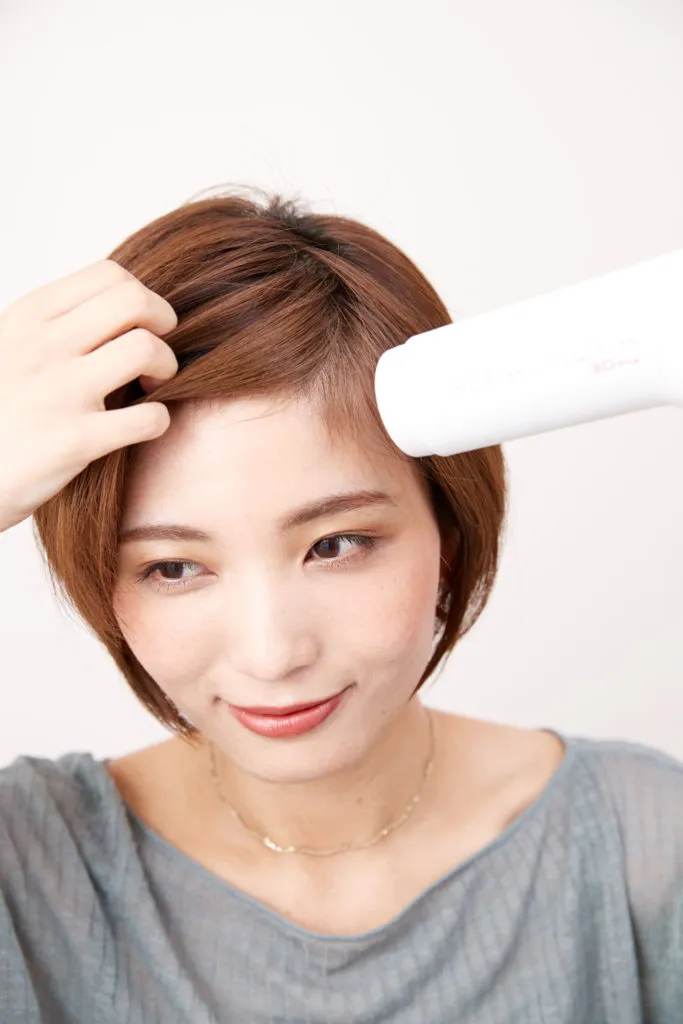 ショートヘアから伸ばしかけの女性が普段の分け目とは逆方向にドライヤーを当てて手ぐしでドライしてヘアアレンジをしている