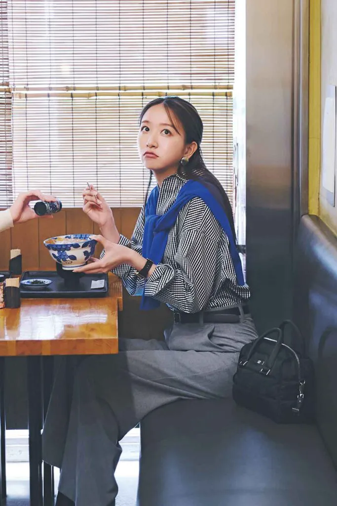 グレーのギンガムチェックシャツにグレーのパンツ、青のニットを肩がけしたコーデ