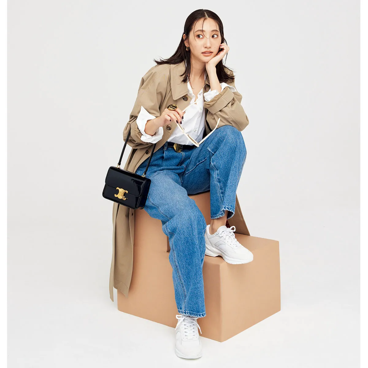 トレンチコートにデニム、白スニーカーを履いた女性