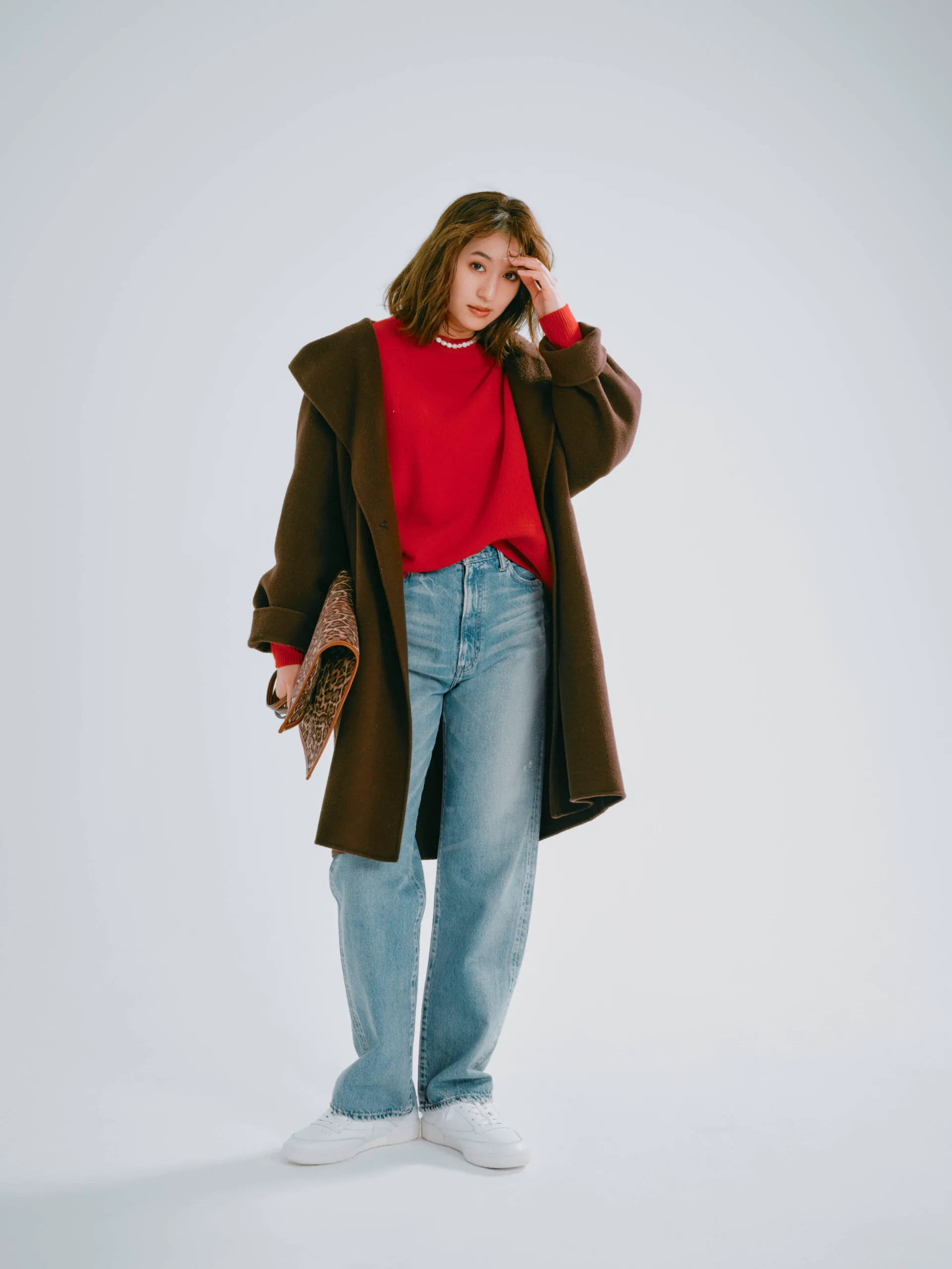 ブラウンのコート、赤ニット、デニムに白スニーカーを履いた女性