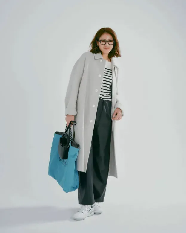 グレーのステンカラーコートにカーキのパンツ、白スニーカーを履いた女性