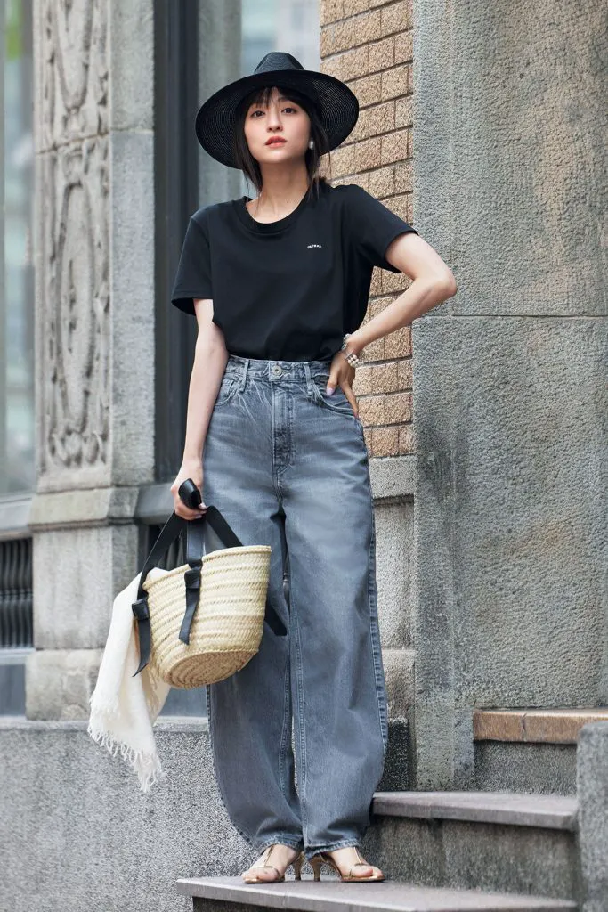 黒Tシャツにカーヴィーデニム、サンダル、ハット、かごバッグを合わせた女性