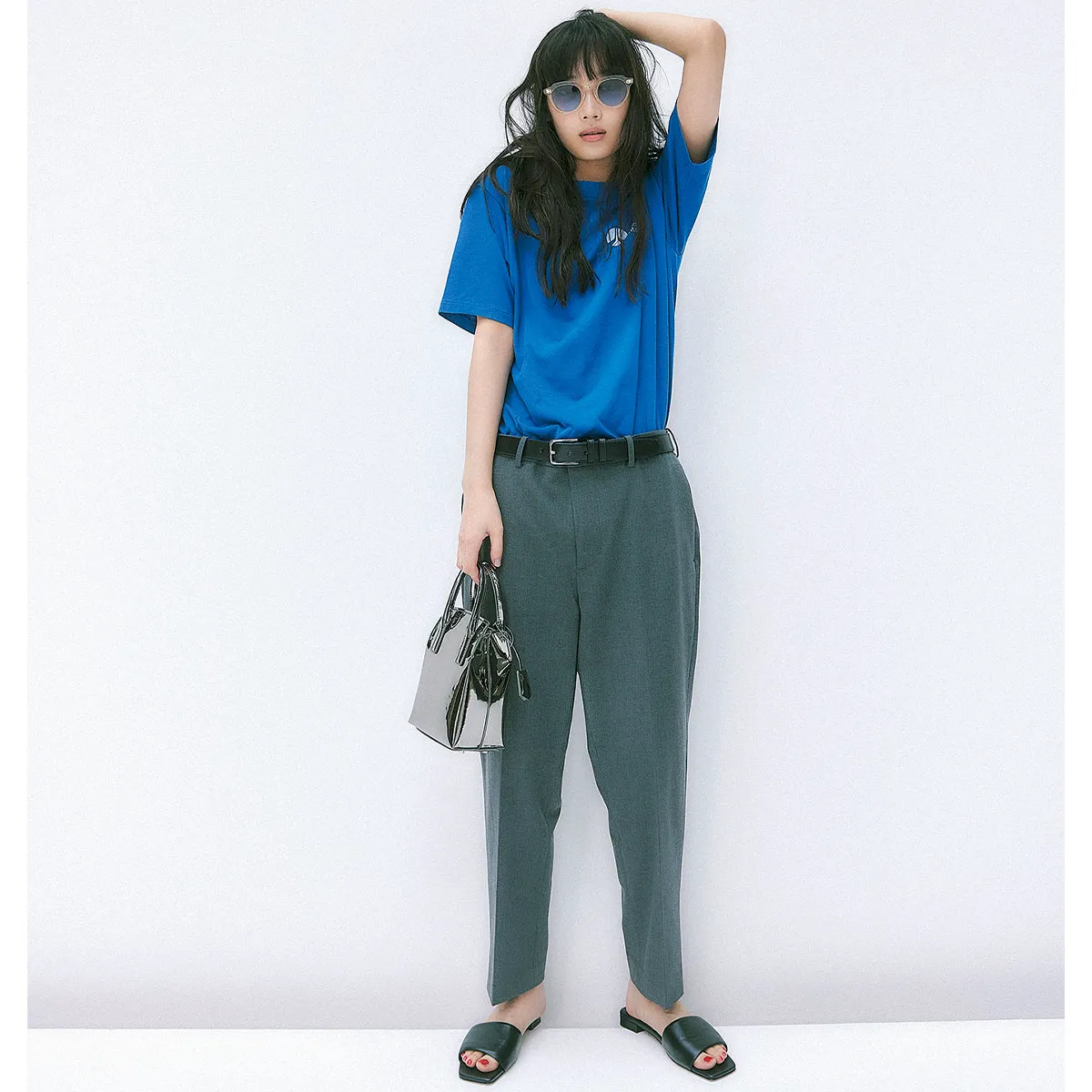ブルーのTシャツ、グレーのアンクルパンツ、黒のフラットサンダルを履いた女性