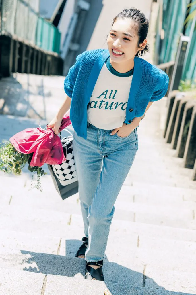 ロゴTシャツにブルーのカーディガン、デニム、サンダルを履いた女性