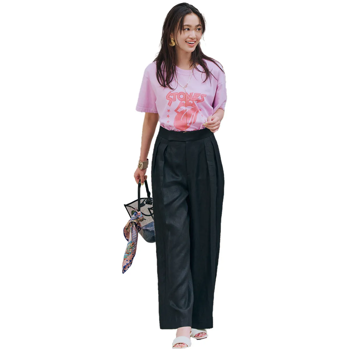 ピンクのロックTシャツ、黒のワイドパンツ、サンダルを履いた女性