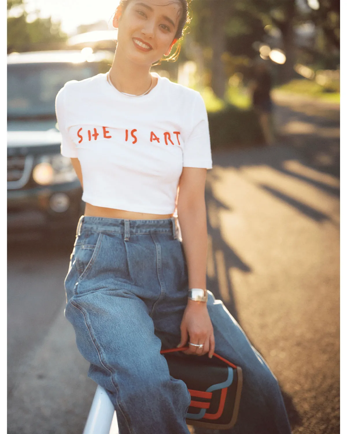 クロップドTシャツ、デニム、ハンドバッグを合わせた女性