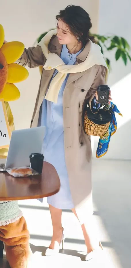 ブルーのシャツワンピース、トレンチコート、パンプスを履いた女性