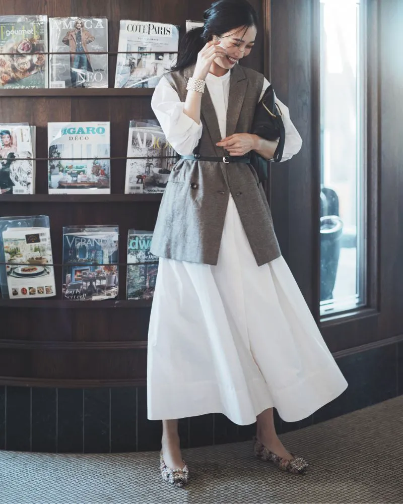 白のシャツワンピース、ジレ、フラットシューズを履いた女性