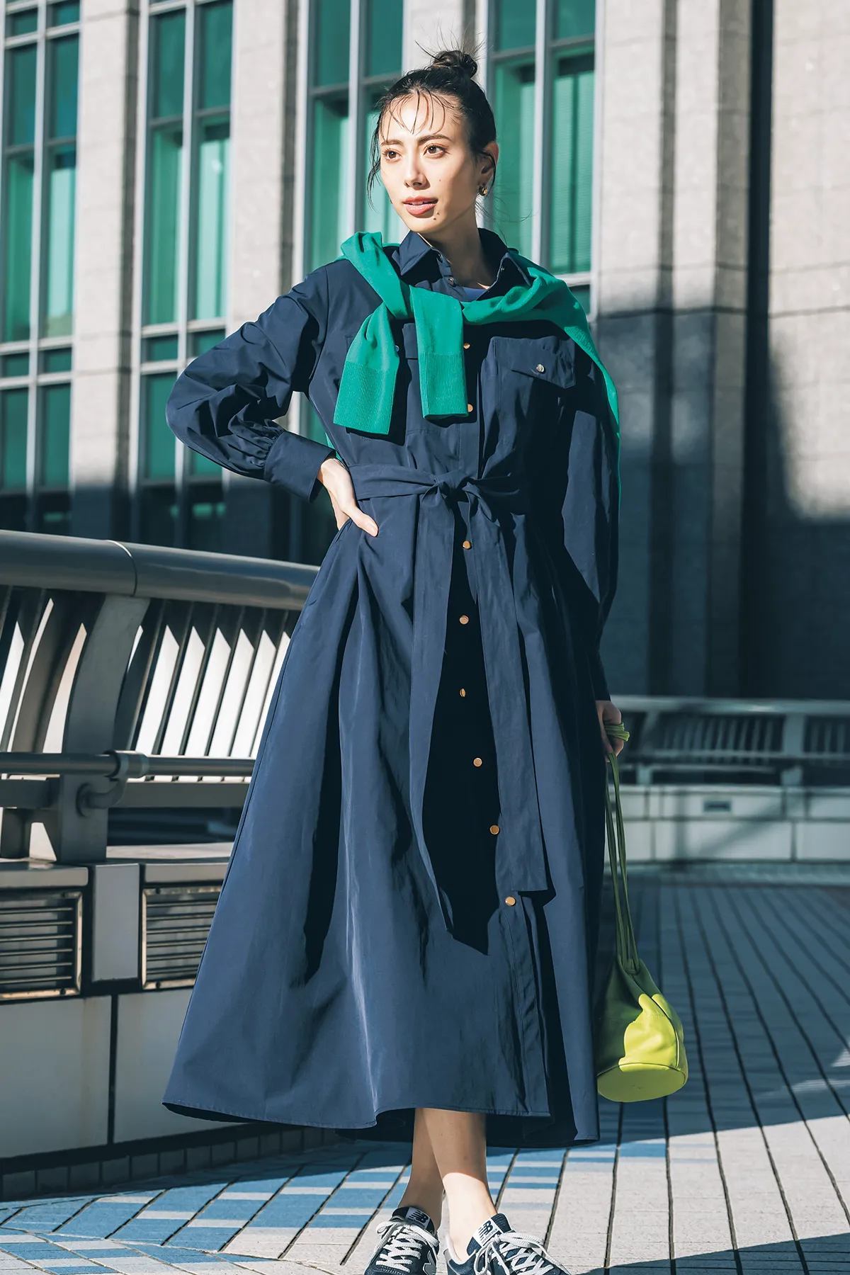 ネイビーのシャツワンピースにグリーンのニットを肩がけ、スニーカーを履いた女性