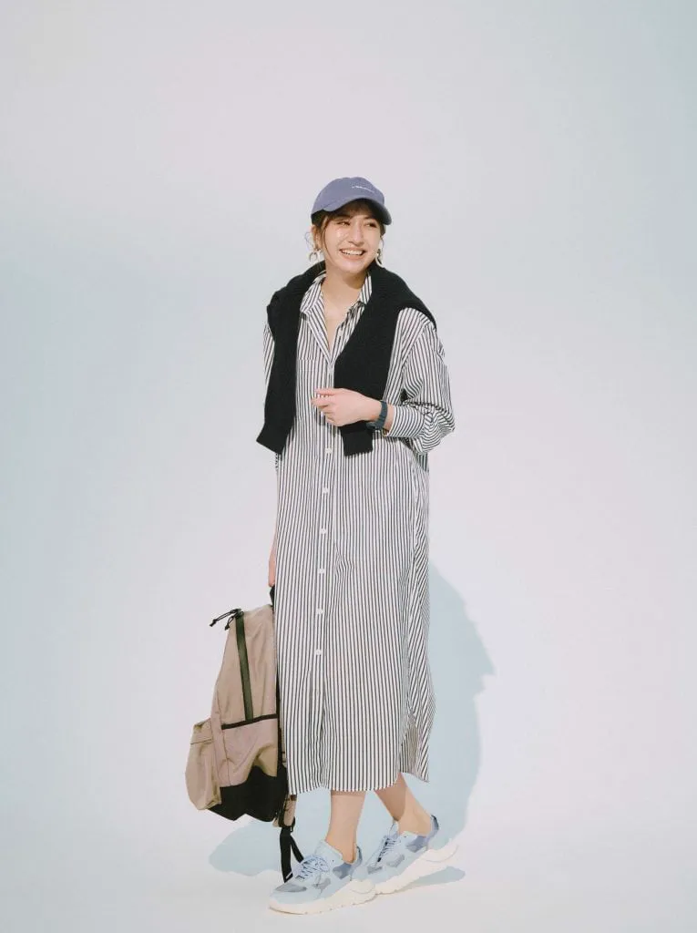 ストライプのシャツワンピースに黒ニットを肩がけ、キャップスニーカーを合わせた女性