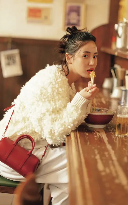 上下白のコーデでボアカーディガンを羽織り、赤いバッグを持った女性