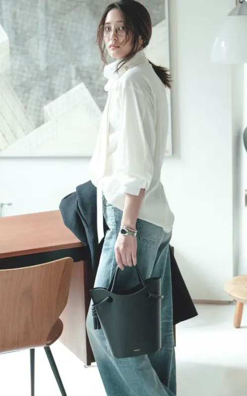 白のボウタイブラウス、デニムパンツコーデに、黒のバッグを持った女性