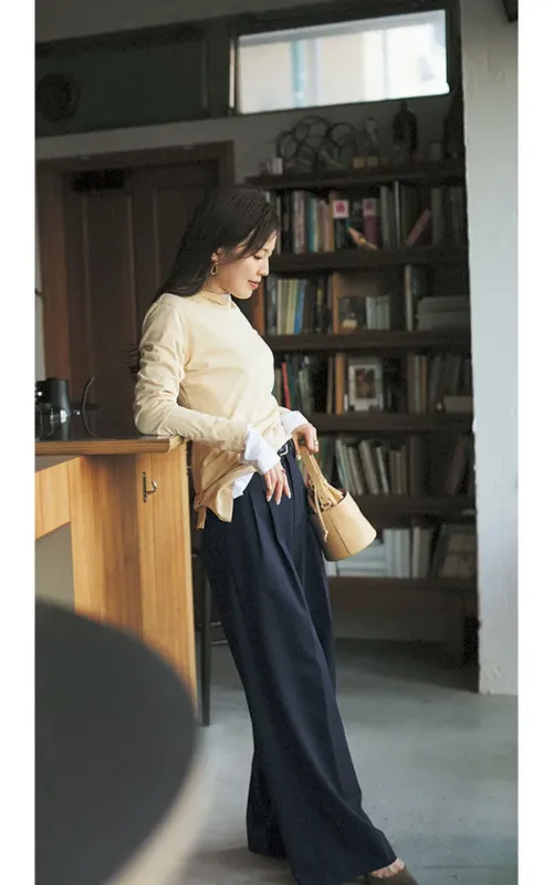 たまご色のトップスと白ロンTでレイヤードし、ネイビーパンツを合わせたコーデの女性