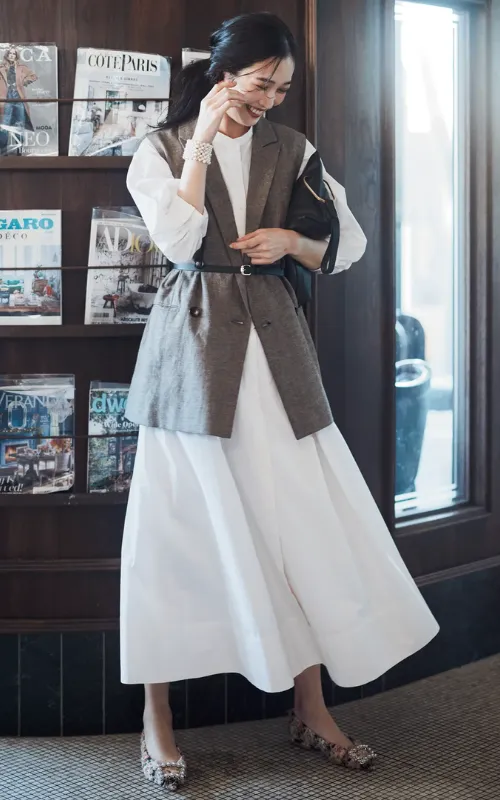 白ワンピース、ブラウンのジレに、ベルトでウエストマークしてスタイルアップしている女性